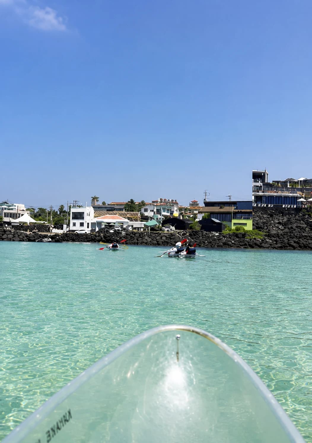 Clear water and Aewol's seaside village seen over the bow of a transparent kayak