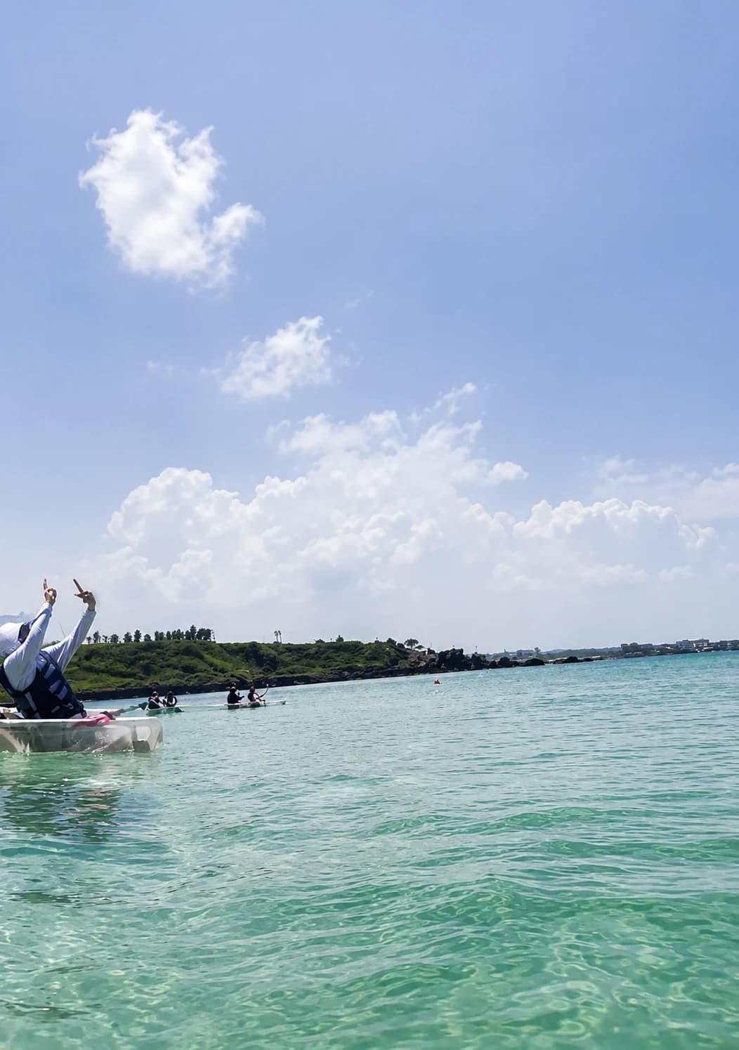 People in transparent kayaks on the clear sea beside Aewol's volcanic coast