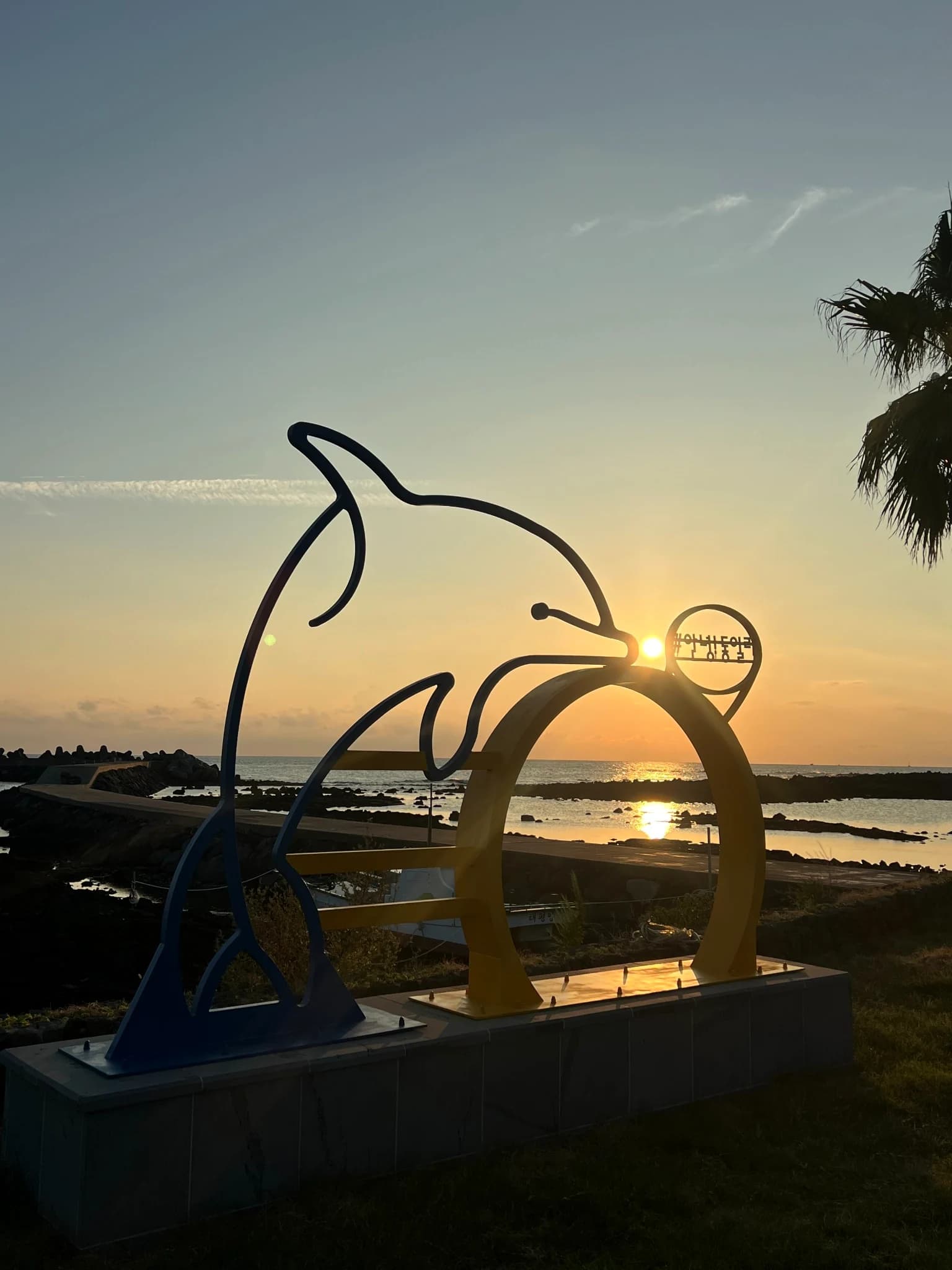 A dolphin sculpture beside Noeul Coastal Road at sunset in southwest Jeju