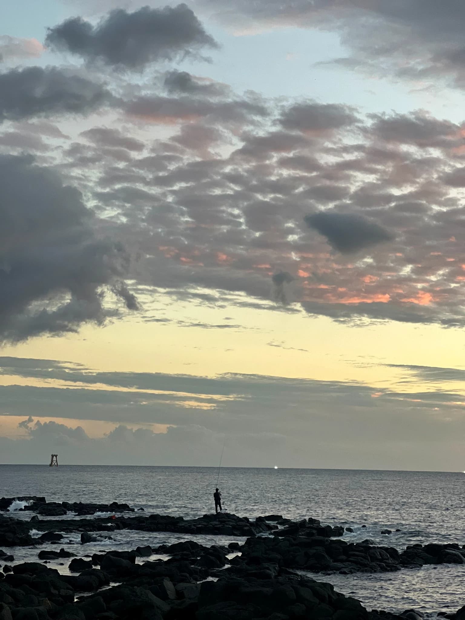 A person fishing from the volcanic shoreline beneath evening clouds at Yeongnak-ri Breakwater