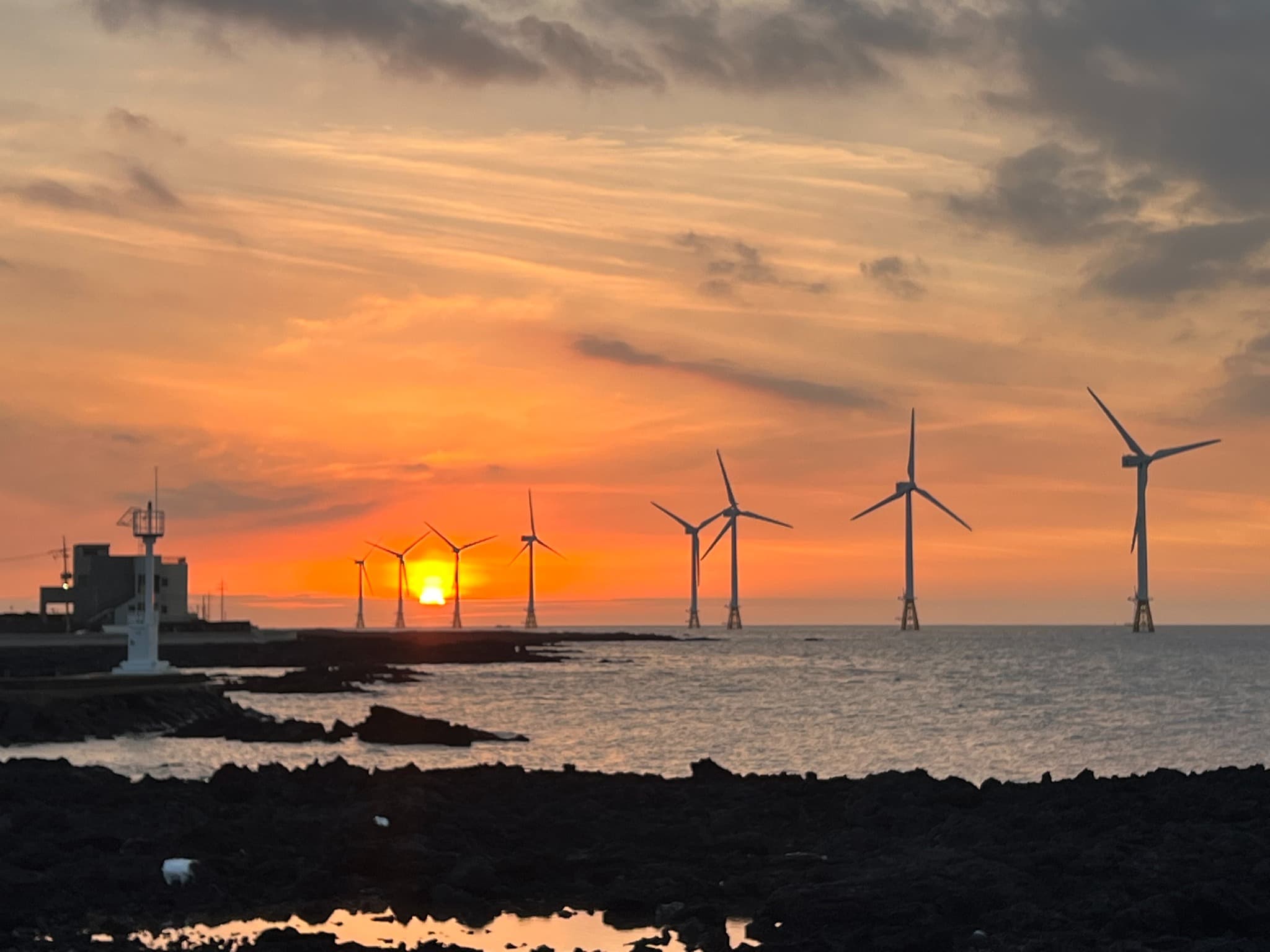 Wind turbines along Jeju’s eastern coast beneath an orange sunset