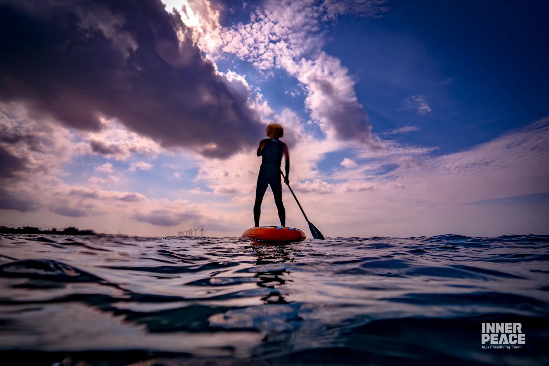 Lee Deokwon standing on a SUP board in the Jeju sea with the original INNER PEACE credit