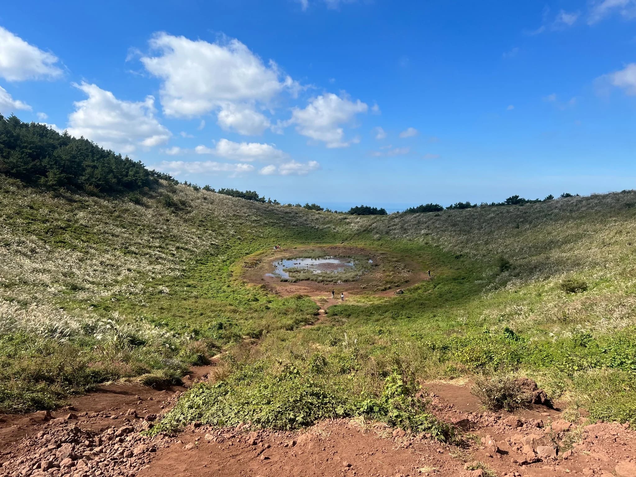 The broad crater of Geum Oreum beneath a bright blue sky in western Jeju
