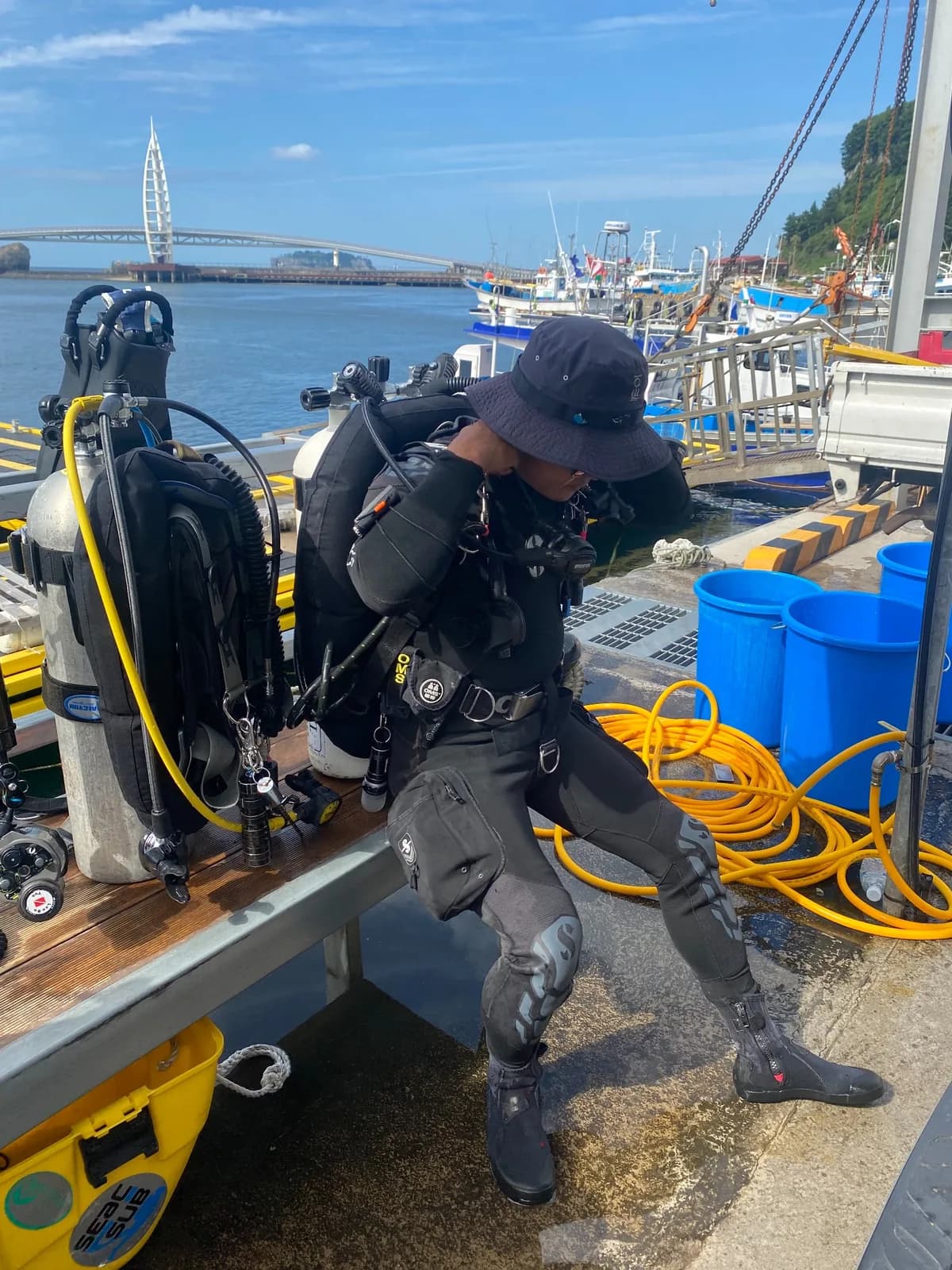 A diver preparing equipment on the dock with Saeyeongyo Bridge behind
